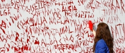 En la imagen, una mujer escribe nombres de mujeres maltratadas en un mural de denuncia